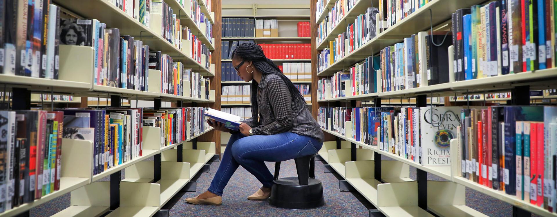 Woman sitting in rows of books reading