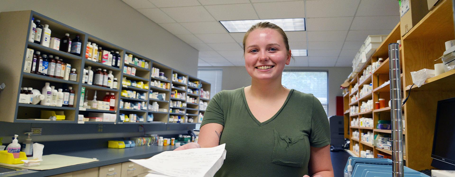 student working in pharmacy lab extends a filled prescription