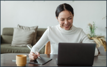 Smiling woman sitting behind laptop taking notes