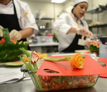 Rose made from carrot shavings with culinary students in background artfully carving watermelons
