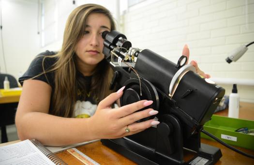 student looking closely into optical equipment to adjust glasses