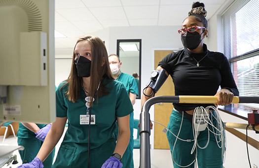 a student watches an EKG monitor while another walks on a treadmill in lab