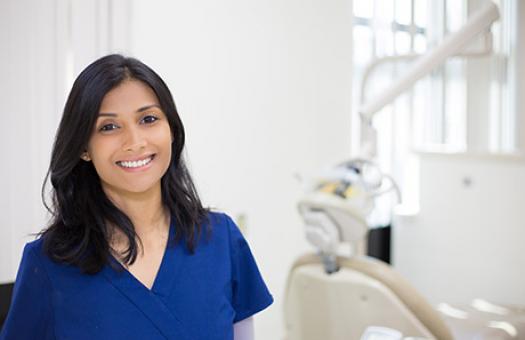 person in scrubs standing in forefront with dental chair in background