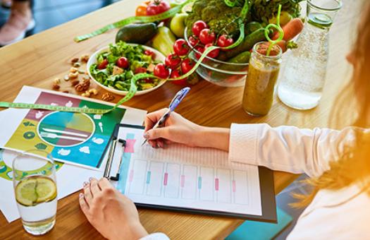 dietitian surrounded by fruits and vegetables writing a meal plan 