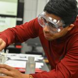 A male student in the Associate in Science program pours liquid into a beaker in a chemistry classroom.