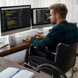 student in a wheelchair works at computer desk with dual monitors